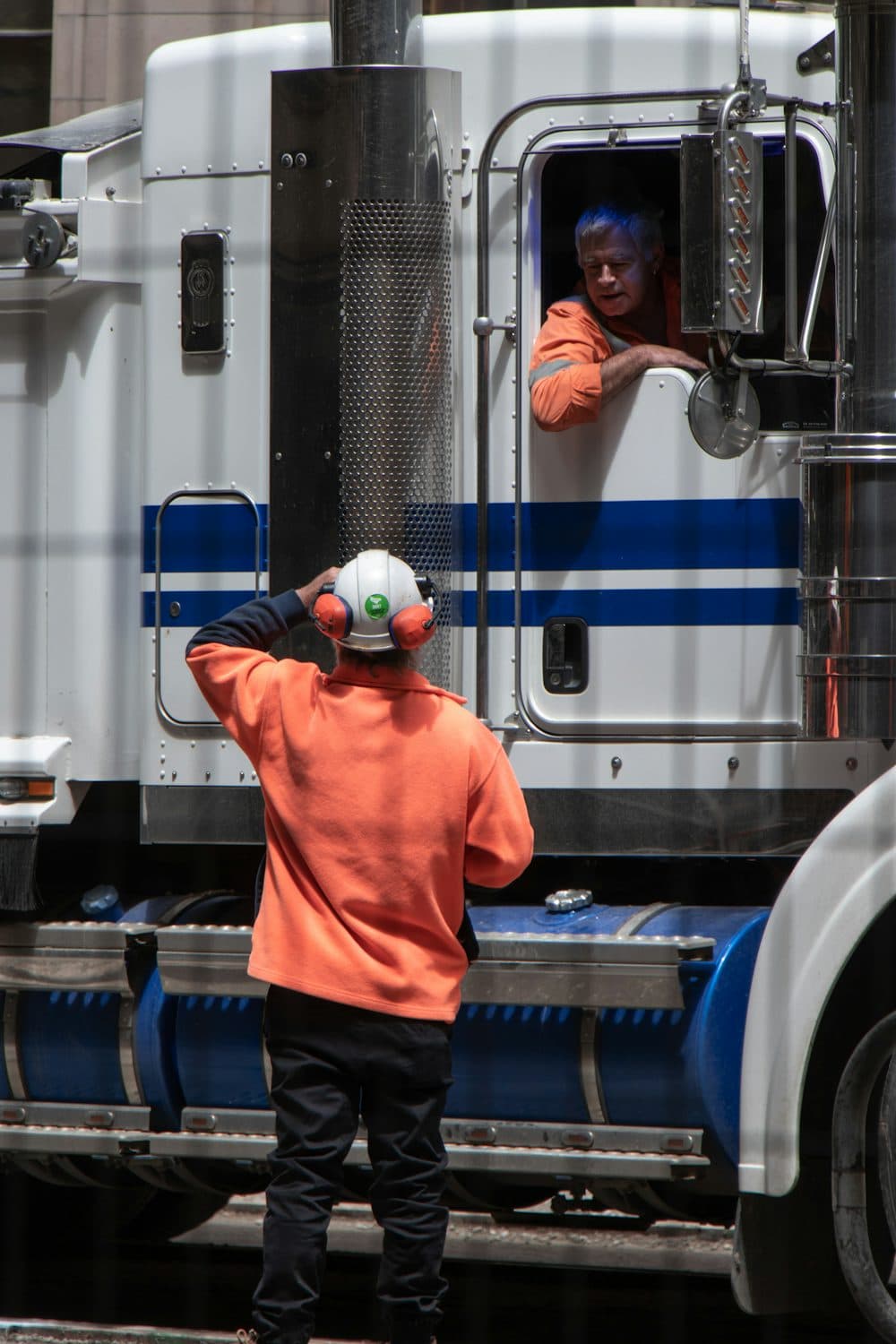 A coordinator in orange talking with a truck driver leaning from the cab
