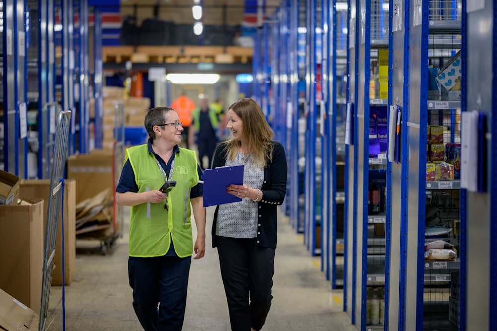 Two workers walking a warehouse aisle with a scanner and clipboard