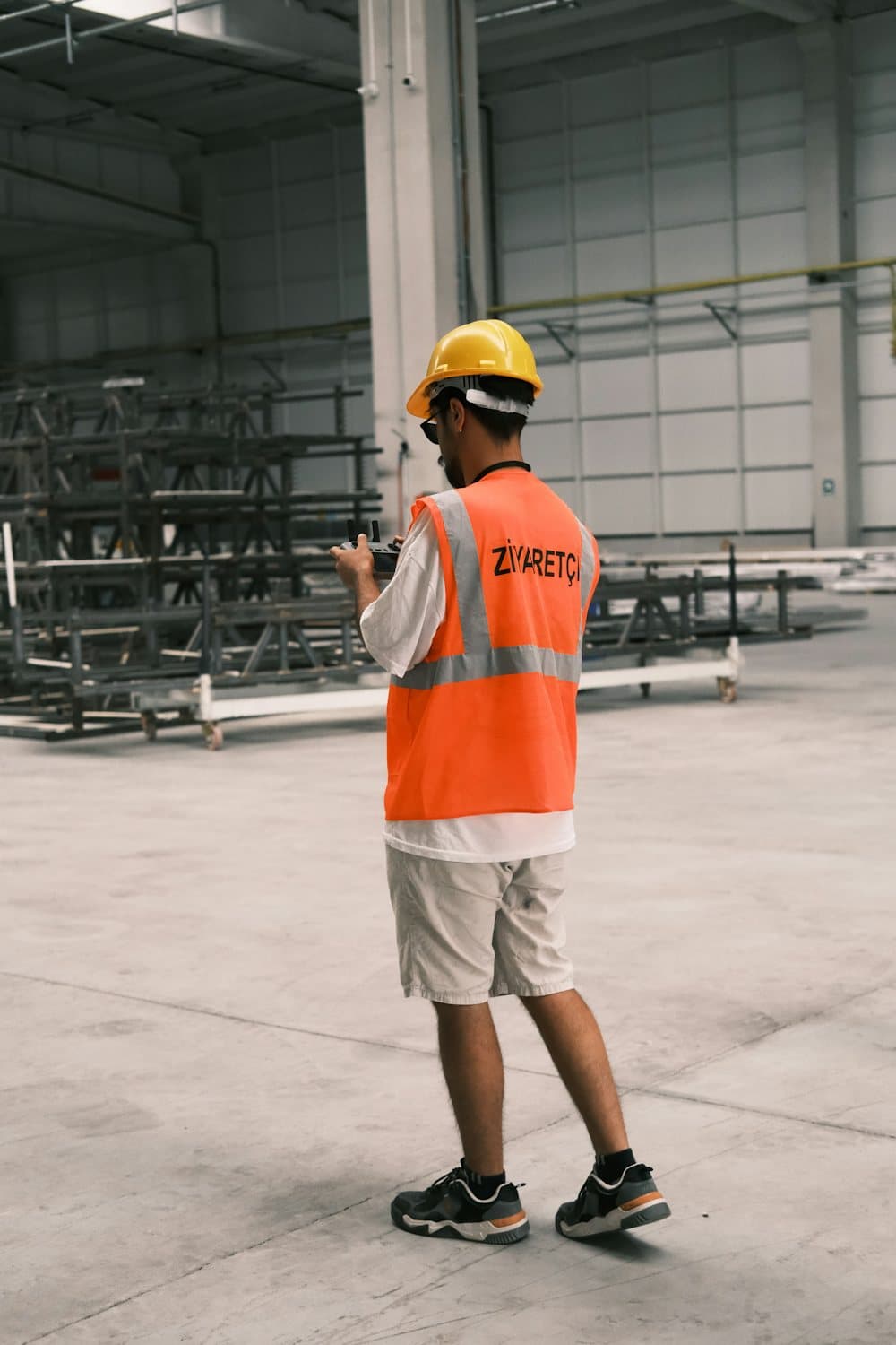 A worker in an orange safety vest and hard hat on a warehouse floor